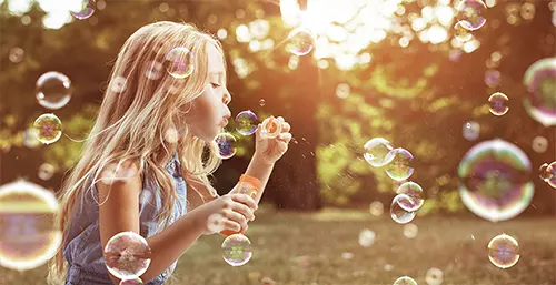 Stres u dzieci - jak sobie z nim poradzić? Dziewczynka puszcza bańki mydlane w letniej scenerii.