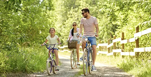 Niedobór witaminy D u dzieci - jak rozpoznać, że dziecko ma za mało witaminy D? Mama, tata i córeczka na przejażdżce rowerowej po lesie w letni dzień.