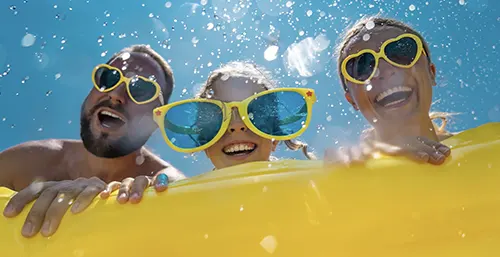 Czy latem podawać dzieciom witaminę D? Kiedy stosować witaminę D latem? Szczęśliwa rodzina na wakacjach - mama, tata i córeczka - kąpie się w basenie, mając na nosie duże okulary w żółtej ramce.