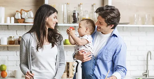 Jakie witaminy i minerały na mocne i zdrowe kości u dzieci? Mama, tata i niemowlę szykują wspólnie obiad w kuchni.